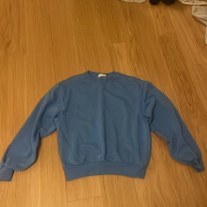 Blå sweatshirt med rund hals - En stilren blå sweatshirt med rund hals och ribbade muddar vid ärmslut och nederkant. Tröjan har en klassisk passform och är tillverkad i mjuk bomull, perfekt för chill dagar. Enkel design utan mönster eller detaljer, passar dig som gillar cleana vibes.
