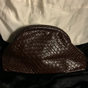 Brun kuvertväska i mönstrat skinn - Snygg brun kuvertväska i skinn med ett coolt präglat mönster som ger en lyxig känsla. Väskan har en mjuk form och öppnas med guldfärgade detaljer. Perfekt för dig som vill ha en unik accessoar med stil. Längd 30 cm 🩷Bredd 8,5 cm 💞 Höjd 17 cm 💗