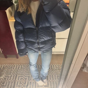 Blå pufferjacka från The North Face - Säljer en mörkblå pufferjacka från The North Face med dragkedja framtill och hög krage. Jackan är vadderad och har långa ärmar samt logga på bröstet. Perfekt för kalla dagar och riktigt snygg till jeans. Se defekt på sista bilden!!