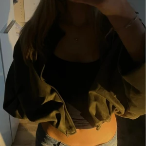 Olivgrön croppad bomberjacka - Säljer en olivgrön croppad bomberjacka med dragkedja framtill. Jackan har loose passform, klassisk krage och långa ärmar. Perfekt för dig som vill ha en chill och trendig look. Materialet känns som syntet och jackan är enkel att matcha med jeans eller kjol.