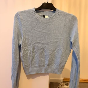 Ljusblå stickad tröja från Divided - Säljer en ljusblå stickad tröja från Divided. Tröjan har rund halsringning, ribbade muddar och är croppad i modellen. Perfekt för lager-på-lager och passar snyggt till både jeans och kjol.