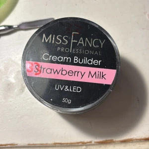 Miss Fancy Cream Builder Strawberry Milk - Miss Fancy Professional Cream Builder i färgen Strawberry Milk, 50g. En mjuk, krämig gel i ljusrosa nyans som används för att bygga och forma naglar med UV/LED-lampa. Kommer i en rund svart burk med rosa etikett. Perfekt för dig som gillar söta och fräscha naglar. Endast swatchad💕