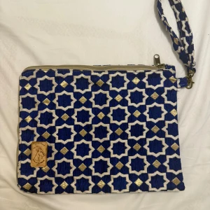 Datorväska handgjord - Snygg datorväska med orientaliskt mönster i blått, guld och vitt. Väskan har en praktisk handledsrem och dragkedja upptill. Insidan är beige med en innerficka. Made in marakech