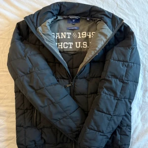 Mörkblå quiltad jacka från GANT - Mörkblå fodrad jacka från GANT med quiltad design och dragkedja framtill. Jackan har ståkrage, två sidofickor med dragkedja och broderad GANT-logga på bröstet. Perfekt för kalla dagar. För liten för mig! Storlek M men passar perfekt till S.