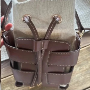 Brun och beige axelväska med snörning - Snygg axelväska i bucket-modell med brunt skinn och beige tyg. Väskan har coola detaljer med snörning upptill och kontrastsömmar. Justerbar axelrem i skinn och guldfärgade metalldetaljer. Perfekt storlek för det viktigaste och unik design som sticker ut.