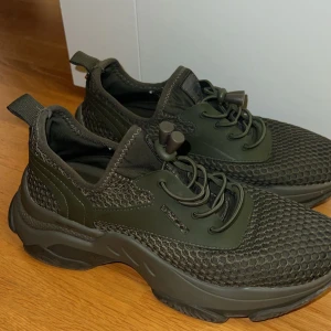 Olivgröna sneakers från Steve Madden - Säljer ett par chunky olivgröna sneakers från Steve Madden med cool meshstruktur och elastisk snörning med dragsko. Skorna har en robust sula och detaljer i syntetmaterial som ger en sportig vibe. Perfekta för dig som gillar streetstyle och vill sticka ut.