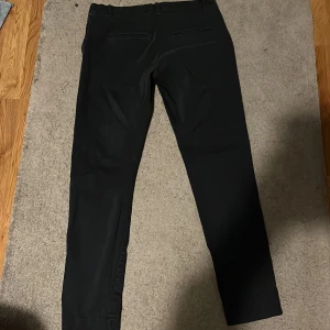 Svarta kostymbyxor från Morris - Stilrena svarta kostymbyxor från Morris med smal passform. Byxorna har två bakfickor med diskreta ficklock och bälteshällor i midjan. Perfekta till skjorta eller stickad tröja för en clean look.