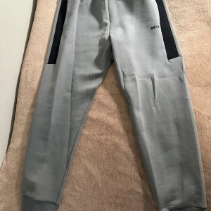 Grå hoodie från BOSS med svarta detaljer - Snygg grå hoodie från BOSS med svarta detaljer längs ärmarna och dragkedja framtill. Storlek S men passar även M då den är stor i storleken. Pris kan diskuteras vid snabb affär.