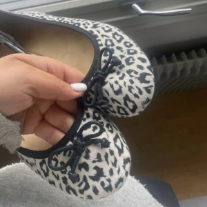 Leopardmönstrade ballerinaskor med rosett - Snygga ballerinaskor från H&M i vitt och svart leopardmönster. Skorna har rund tå, svarta kanter och en söt liten rosett framtill. Perfekta för dig som vill sticka ut med ett djurmönster. Platt sula och mjukt tygmaterial för skön känsla.
