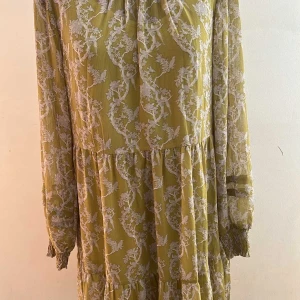 Gul blommig långklänning Coster Copenhagen - Säljer en gul långklänning från Coster Copenhagen med vitt blommigt mönster. Klänningen har långa ärmar med smock vid ärmslut, rundad hals med liten volangkant och knappdetalj framtill. Materialet är lätt och har ett innerfoder i satinliknande tyg.