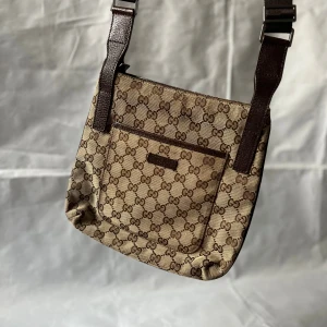 Gucci väska – klassisk beige/brun canvas & läderdetaljer - ✨ Speciella detaljer: Tidlös Gucci-design i beige canvas med bruna läderdetaljer, justerbar axelrem och ikonisk GG-stil. 🎨 Färg: Beige / Brun 📏 Storlek: ca B 27 × H 25 × D 5 cm 🪡 Rem: Justerbar axelrem 🇮🇹 Tillverkad i: Italien ♻️ Skick: Gott vintageskick – lätta spår av användning på hörn och rem, men inga större defekter. Invändigt rent och välskött. 🎁 Tillbehör: Inga (ingen dust bag eller ask – endast väskan som på bild). ‼️ Skickas dagen efter köp ‼️