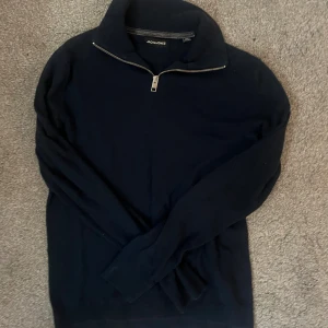 Marinblå half zip tröja Jack & Jones - Snygg marinblå långärmad tröja från Jack & Jones med half zip-dragkedja vid kragen. Tröjan har en stilren design med ribbade muddar och är tillverkad i mjuk bomull. Perfekt för dig som gillar enkel och klassisk stil.