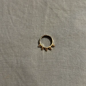 Guldfärgad ring med spetsiga detaljer - Cool ring i guldfärg med fyra spetsiga, pyramidformade detaljer runt hela ringen. Perfekt för dig som gillar edgy och unik design. Ringen är i metall och har en modern vibe som sticker ut bland vanliga smycken.