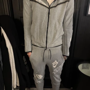 Nike tech set - Säljer knappt använda gråa mjukisbyxor från Nike med vita tryck och loggor på benen. Grå matchande Nike tech tröja till. Storlek i byxorna är XS och storlek i tröjan är S. Produkten finns på flera sidor.