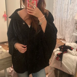 Svart kappa från Stockh lm - Säljer en svart kappa från Stockh lm med lös och oversized passform. Jackan har en klassisk krage, knappar framtill och är helfodrad med glansigt tyg. Perfekt för höst och vinter, enkel att styla till olika outfits.