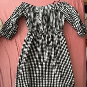 Svartvit rutig offshoulder klänning - Säljer en svartvit rutig klänning med offshoulder och trekvartsärmar. Klänningen har elastisk midja och är gjord i mjuk bomull. Perfekt för dig som gillar en chill och trendig stil med klassiskt rutmönster.