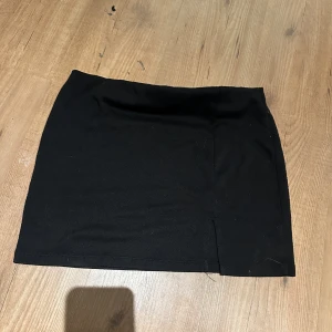 Svart kortkjol från 157 - En enkel svart kortkjol från 157 i storlek L. Kjolen har rak passform med slits och är tillverkad i mjukt material som känns skönt mot huden. Perfekt att matcha med en crop top eller hoodie för en chill look.