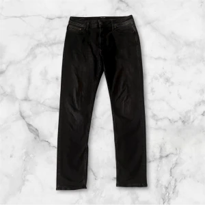 Svarta jeans från Jack & Jones Clark - Svarta jeans från Jack & Jones, modell Clark Regular. Klassisk femficksdesign med raka ben och subtila slitningar. Jeansen har knapp och dragkedja i gylfen samt bälteshällor. Materialet är mjukt denim i bomull med lite stretch för extra komfort. Nypris 899kr: Mitt pris 449kr