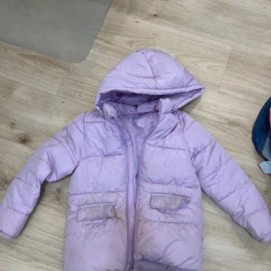 Ljuslila pufferjacka med huva - Säljer en ljuslila pufferjacka från C i storlek 128. Jackan har huva, två fickor med lock framtill och dragkedja. Perfekt för kalla dagar och har en snygg, enkel design som är lätt att matcha med andra plagg. Mycket bra. Köprare betalar för frakten 