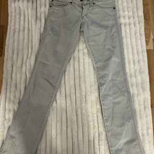 Ljusgrå jeans från Wrangler W27 L32 - Snygga ljusgrå jeans från Wrangler med klassisk femficksdesign och raka ben. Jeansen har detaljerade sömmar, bälteshällor och Wrangler-logga på bakfickan. Tillverkade i bomull för en skön och slitstark känsla. Perfekt för dig som gillar stilrena och tidlösa jeans.