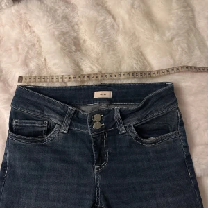 Blå bootcut jeans från Nelly - Snygga mörkblå jeans från Nelly med bootcut passform och låg midja. Jeansen har två knappar fram, klassiska fickor och coola broderade detaljer på bakfickorna. Materialet är jeans med lite stretch för skön passform.