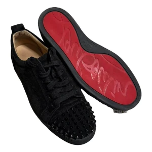 Christian Louboutin svarta sneakers strl 40 - Svarta sneakers från Christian Louboutin med ikonisk röd sula och snörning. Ovandelen är i mocka och tån är täckt med svarta nitar för en edgy look. Rund tå och platt sula. Perfekt för dig som vill sticka ut med lyxiga detaljer.