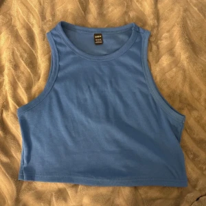Blå croppad linnetopp  - Säljer en blå croppad linnetopp från shein i storlek L. Toppen är ribbad och ärmlös med rund halsringning. Perfekt för dig som gillar enkel och stilren design. Materialet är mjukt och stretchigt, vilket gör den skön att bära.
