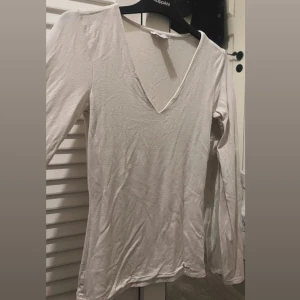 Vit långärmad v-ringad topp - Säljer en enkel och stilren vit långärmad topp från KappAhl med djup v-ringning. Toppen är gjord i mjuk bomull och har en smickrande normal passform. Perfekt att matcha med jeans eller kjol för en clean look.