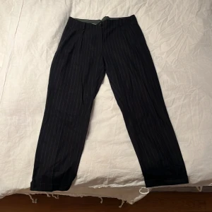 Randiga kostymbyxor från J.Lindeberg - Snygga mörkblåa kostymbyxor från J.Lindeberg med tunna vita ränder. Byxorna har rak passform och är tillverkade i en skön blandning av ull, polyester och elastan.