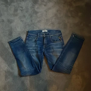 Blå Replay jeans, storlek 29/30 - Snygga blå jeans från Replay med klassisk femficksdesign och diskreta slitningar. Jeansen har normal passform, raka ben och medelblå tvätt. Perfekta för dig som gillar en stilren och avslappnad look. 