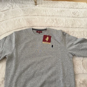 Grå sweatshirt från MCS - Säljer en stilren grå sweatshirt från MCS i storlek S. Tröjan har rund halsringning och en liten svart broderad logga på bröstet. Perfekt för en avslappnad och snygg look. Tillverkad i mjuk bomull för extra komfort.