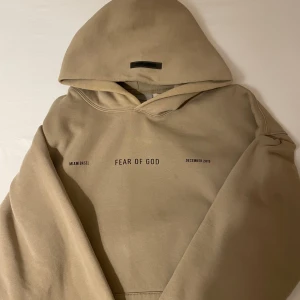 Beige hoodie Fear of God Rituals Essentials  - Säljer en beige hoodie från Fear of God Essentials äkta. med tryck på bröstet och stor grafisk print på ryggen med texten 'RITUALS'. Hoodien har stor huva, ribbade muddar och avslappnad passform. Perfekt för dig som gillar streetwear och unika designer. Väldigt bra skick!  Pris kan diskuteras!!   