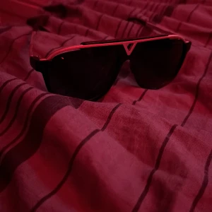 Svarta solglasögon med röd detalj - Snygga svarta solglasögon med en röd ram upptill och cool V-formad detalj i mitten. Glasen är mörka och modellen har en sportig vibe som passar perfekt till sommardagar.