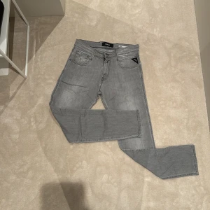 Grå Replay jeans (ANBASS) slim fit - Snygga grå jeans från Replay med klassisk femficksdesign och raka ben. Jeansen har svarta kontrastsömmar, Replay-logga på bakfickan och patch bak i midjan. Perfekta för dig som gillar en clean och stilren look. Dessa jeans är i mycket bra skick och är i strl 30.