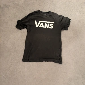 Svart Vans t-shirt med logga - Svart t-shirt från Vans med stor vit logga på bröstet. Klassisk rund halsringning och korta ärmar.