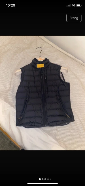 Svart dunväst från Parajumpers - Säljer en svart dunväst från Parajumpers, modell Super Lightweight. Västen har quiltad design, hög krage med gul detalj, två fickor med dragkedja och insida i silvergrått. Perfekt för lager-på-lager och riktigt snygg till höst och vinter.