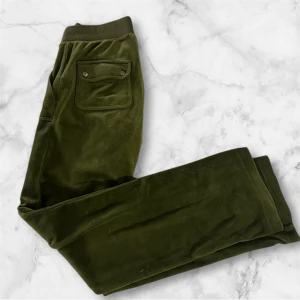 Olivgröna Juicy Couture XS - Snygga olivgröna mjukisbyxor från Juicy Couture. Byxorna har bred resårmidja med snörning, fickor fram och  bakficka med knappdetalj. Perfekta för chill och streetstyle, med klassisk Juicy Couture-logo på ena fickan. Använd få tall gånger 