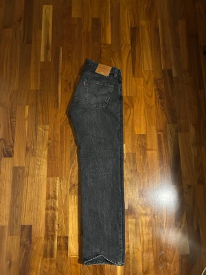 Levi's 501 svarta jeans W32 L32 - Klassiska svarta Levi's 501 jeans med rak passform och knappgylf. Jeansen har fem fickor, tydlig Levi's-lapp bak och röd etikett på bakfickan. Tillverkade i robust denim som ger en tidlös look.