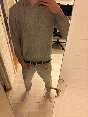 Grå hoodie från Bvaldi med brodyr - Snygg grå hoodie från Bvaldi i mjukt material med dragsko i huvan och broderad logga på bröstet. Klassisk passform med ribbade muddar vid ärmslut och nederkant. Perfekt för en chill och stilren look.