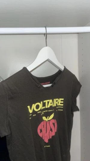 Svart t-shirt Zadig & Voltaire - Cool mörk grökt-shirt från Zadig & Voltaire med tryck i gult och rött framtill och turnélista på ryggen. Rund hals med råa kanter och två svarta knappar vid halsen. Materialet är mjuk bomull och passformen är normal. Nypris ca 800, nästan aldrig använd.