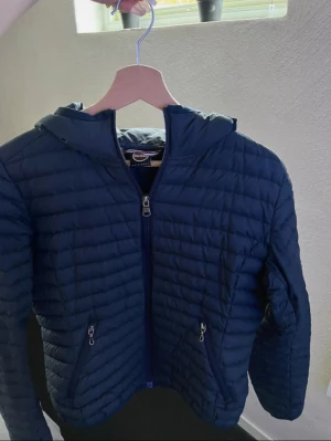Mörkblå dunjacka från Colmar - Snygg mörkblå dunjacka från Colmar med huva. Jackan har två sidofickor med dragkedja och hel dragkedja framtill. Perfekt för kyliga dagar och har en stilren look som funkar till många outfits. Gammal model där av inte identisk därav mitt pris, inga defekter!