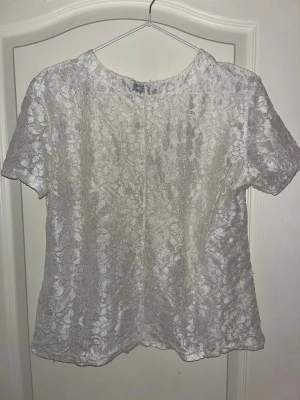 Vit blommig blus  - Säljer en vitfärgad blus från Vittoria, tillverkad i Italien. Blusen har ett blommigt spetsmönster, rund halsringning och korta ärmar.  Ger en lyxig känsla. Perfekt för dig som vill sticka ut med något unikt och snyggt.