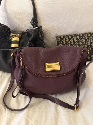 Burgundy Q Classic Natasha bag! - Snyggaste burgundy/lila handväskan i äkta läder från Marc by Marc Jacobs. Den ikoniska modellen Q Classic Natasha! En populär och eftertraktad vintagemodell med gulddetaljer och justerbart band. Som ny i skicket!🤍 Det här är en tidlös modell som inte längre finns att köpa, vilket gör den extra eftertraktad. Perfekt för dig som vill ha en stilren tidlös väska med riktigt bra andrahandsvärde. Passar lika bra till vardag som till fest. Kan hämtas hemma hos mig i Nacka eller skickas 🤍