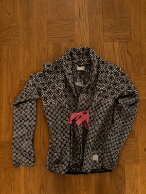 Mönstrad kofta från Odd Molly - Säljer en svartvit kofta från Odd Molly med snyggt geometriskt mönster och lång ärm. Koftan har en rosa knytning i midjan.