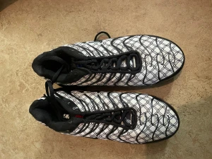 Nike Air Max Plus Tn svart/vit mönstrad - Nike Air Max Plus Tn sneakers med svart och vit färg, coolt rutigt mönster på ovandelen och svarta detaljer. Sulan har synliga Air-enheter och Tn Air-logga på hälen. Skorna har snörning och en platt sula, tillverkade i syntet och textil.