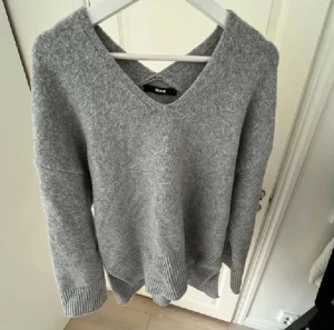 Grå stickad v-ringad tröja Bikbok - Mysig grå stickad tröja från Bikbok i storlek S. Tröjan har v-ringad hals och breda ribbade muddar vid ärmslut och nederkant. Den är perfekt för kyliga dagar.