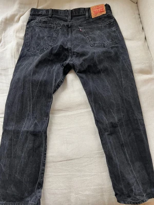 Levi's 501 svarta jeans W38 L32 - Svarta Levi's 501 jeans med klassisk rak passform och femficksdesign. Jeansen har en snygg tvättad look, silverfärgad knapp och nitar samt den ikoniska läderpatchen bak i midjan. Tillverkade i slitstarkt bomullsjeansmaterial.