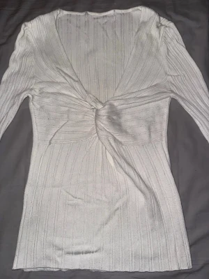 Vit ribbad omlottopp med lång ärm - Säljer en vit ribbad omlottopp med lång ärm och snygg twistad detalj framtill. Toppen har v-ringad hals och är figurnära i modellen. Perfekt för dig som gillar stilrena och trendiga plagg med lite extra detalj. Materialet är mjukt och stretchigt.