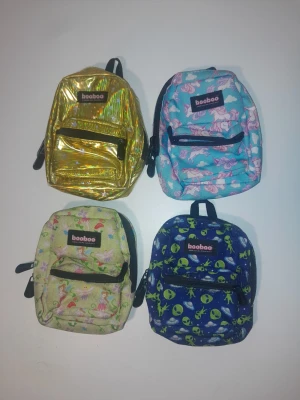 Fyra små ryggsäckar från Booboo - Fyra miniryggsäckar från Booboo med olika mönster: en glittrig guldig, en blå med rosa enhörningar, en ljusgrön med älvor och en marinblå med gröna aliens. Alla har svart dragkedja och justerbara band. Perfekta för småprylar eller som accessoar.