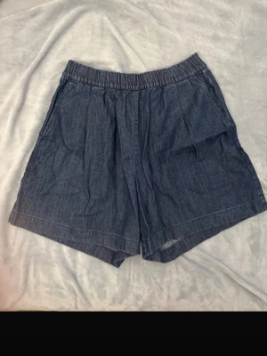 Blå loose & högmidjade shorts från Uniqlo - Säljer ett par blå loose-fit & högmidjade shorts från Uniqlo med elastisk midja och en bakficka. De är tillverkade i en mjuk bomullsblandning med polyester och har en enkel, avslappnad look som passar perfekt till varma dagar. Klassisk design utan mönster.